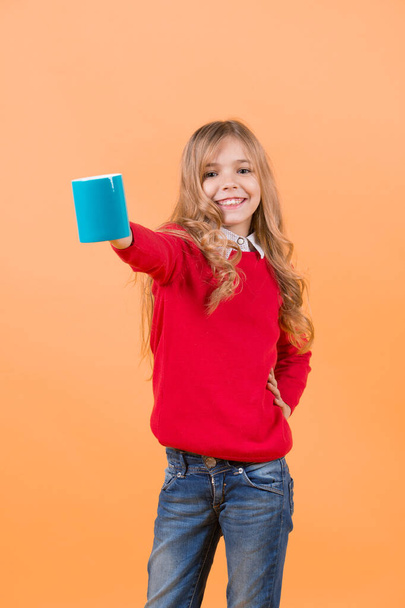 Tea or coffee break. Girl with long blond hair in red sweater hold mug. Thirst, dehydration concept. Health and healthy drink. Child smile with blue cup on orange background. - 写真・画像