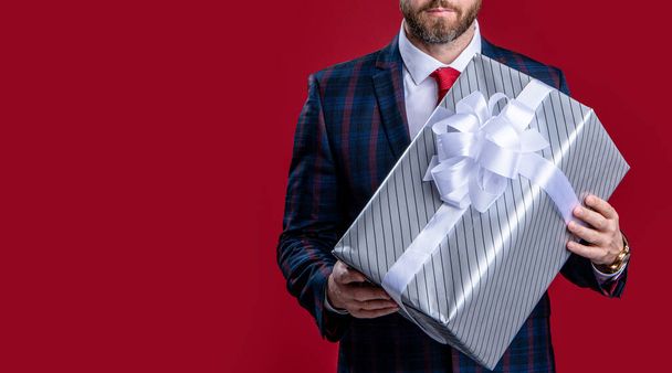 cropped view of businessman with present, copy space. businessman holding present box in suit. businessman with present isolated on red background. businessman hold present in studio. - Fotó, kép