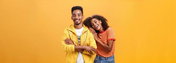 Awesome when boyfriend is best friend. Portrait of charming friendly african american woman leaning on guy touching his shoulder feeling happy they together and she can rely on posing orange wall - Photo, Image