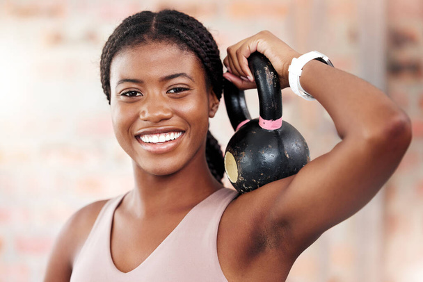 Mujer negra, cara y sonrisa para el ejercicio de kettlebell para el entrenamiento de culturistas, fitness y entrenamiento en el gimnasio para músculos fuertes, salud y bienestar. Retrato de una mujer estadounidense con pesas para entrenar para el poder. - Foto, imagen