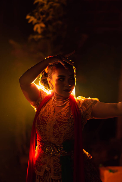 A Silhouette body of a Balinese woman in a traditional orange dress while dancing in front of the lighting on the dark night at the festival - Foto, Imagen