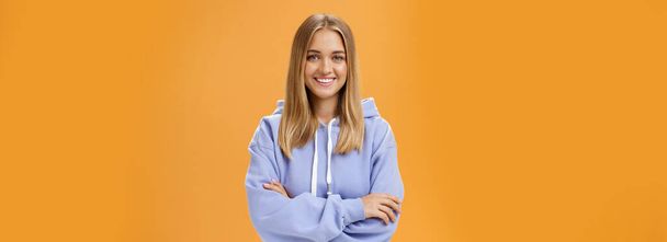Fiatal kreatív és ambiciózus női diák bámult saját projekt otthon dolgozó szabadúszó, amelynek szabadidő és a munka, ha szeretné tartani a kezét keresztbe mellkas visel kényelmes kapucnis narancssárga fal felett - Fotó, kép