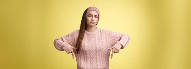 Why me, gosh. Gloomy upset complaining cute glamout young european girl in casual sweater, headband frowning, whining grimacing displeased pointing down, unhappy see lots work over yellow wall. - Фото, изображение