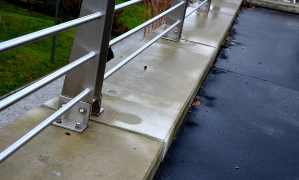 rozsdamentes acél korlát a tetőparkoló betonfalán. Rögzített csavarok a padlás lábához. A fémlemez lecsapolja az esővizet. acélhuzalháló gyermekek elesése ellen - Fotó, kép