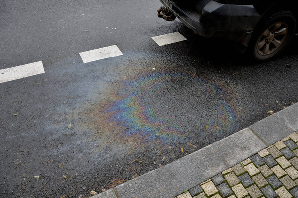 oil stains from leaks in the car engine. oil after rain makes spots with rainbow reflections refractive sun spectrum. beautiful color mosaic on black background parking lot, abstraction, ecology - Photo, Image