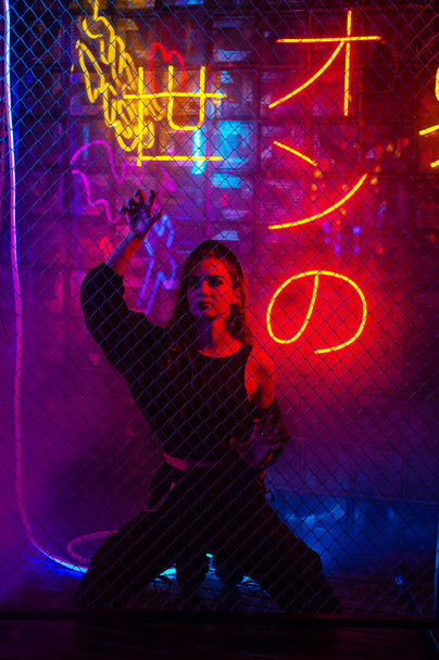 Caucasian woman in neon studio behind chain-link mesh - Foto, afbeelding