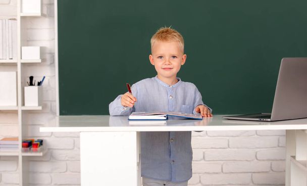 Pupil near chalkboard during lesson at primary school. School child student learn lesson sitting at desk studying - Foto, imagen