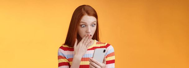 Vrouw ontvangen schokkende bericht hijgende cover mond palm staren smartphone display ontdekt die volgen vriendje internet sociaal netwerk staande verbaasd, oranje achtergrond. - Foto, afbeelding