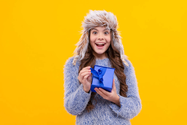 surprised kid with purchase in hat. boxing day. teen girl in knitwear on yellow background. child buy gift. black friday discount. winter shopping sale. birthday present box. christmas season. - Photo, Image