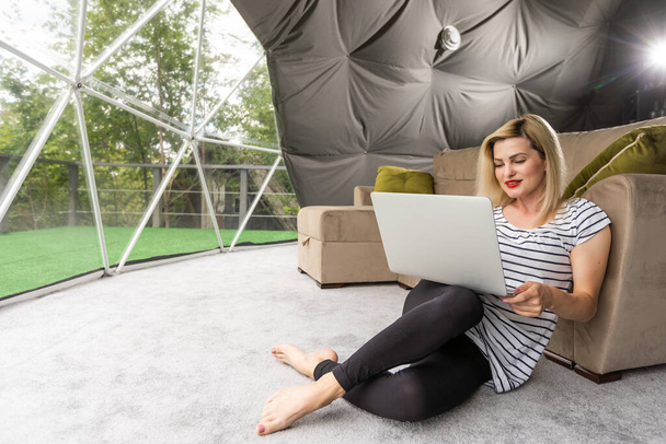 Nuori valkoihoinen nainen, joka käyttää ja katselee kannettavaa tietokonetta telttailuhotellissa. Matkailu, loma ja viikonloppu - Valokuva, kuva