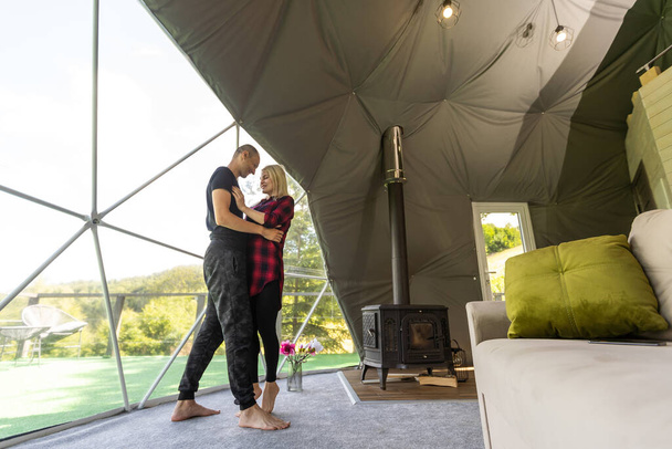 couple looking at nature from geo dome tents. Green, blue, orange background. Cozy, camping, glamping, holiday, vacation lifestyle concept. Scenic outdoors cabin. - Foto, Bild