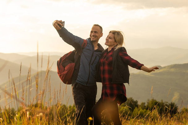 Мужчина и женщина стоят и обнимаются на вершине горы, осенний поход с рюкзаками
. - Фото, изображение