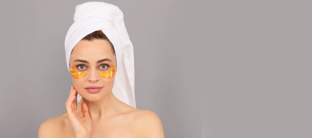Επίθεμα ματιών. αισθησιακή κυρία με πετσέτα terry χρήση προσώπου επίθεμα χρυσό μάτι για το δέρμα, spa. Όμορφη γυναίκα απομονωμένο πρόσωπο πορτρέτο, πανό με μακιγιαρισμένο αντίγραφο χώρο - Φωτογραφία, εικόνα