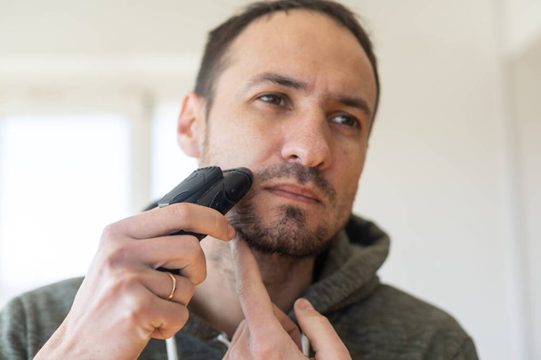 Человек бреется с электрической бритвой - Фото, изображение