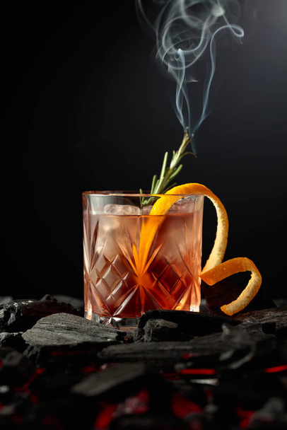 Old-fashioned cocktail with ice, orange peel, and rosemary. Whiskey with a burning twig of rosemary on a dark background. - Zdjęcie, obraz