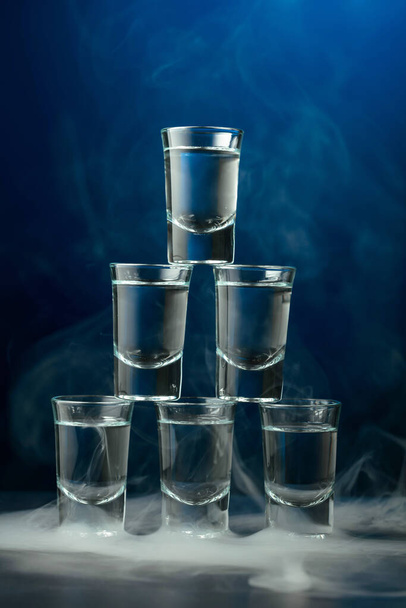 Vasos de vodka en humo sobre fondo azul oscuro. Concepto de bebidas club. - Foto, imagen