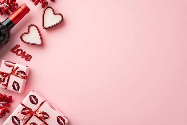 Concepto del Día de San Valentín. Foto vista superior de cajas de regalo en papel de regalo con patrón de labios beso botella de vino velas en forma de corazón e inscripción amor sobre fondo rosa pastel aislado con copyspace - Foto, imagen
