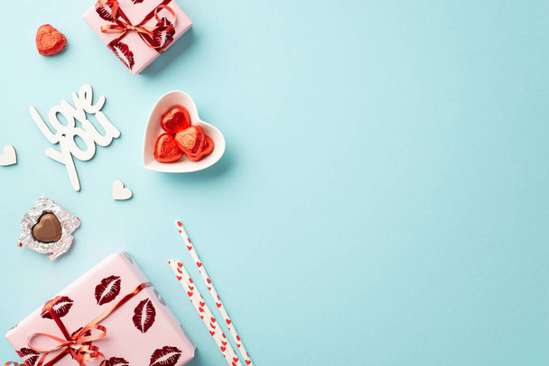 Valentine's Day concept. Top view photo of gift boxes in wrapping paper with kiss lips pattern heart shaped saucer candies straws inscription love you on isolated pastel blue background with copyspace - Φωτογραφία, εικόνα