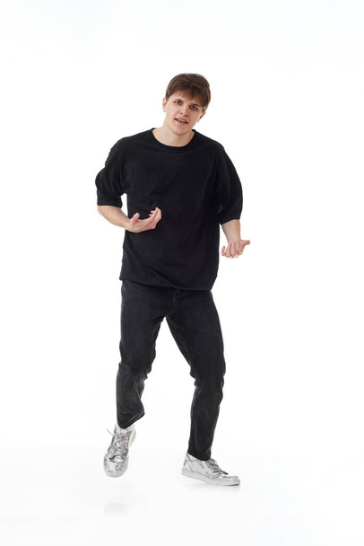 Młody mężczyzna w czarnej koszulce i dżinsach tańczący na białym tle. Pełna długość - Zdjęcie, obraz