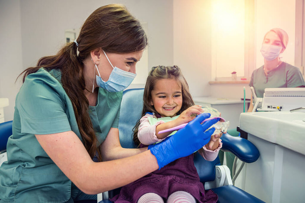 A női fogorvos megmutatja a kislánynak, milyen helyesen mosott fogat. Fogorvosi rendelő - Fotó, kép