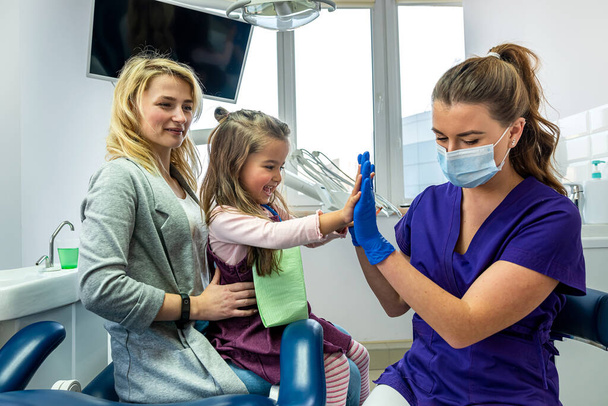 Мати маленької дівчинки і стоматолог заспокоюють маленьку дівчинку перед лікуванням зубів. Концепція підходу до дітей в стоматології
 - Фото, зображення