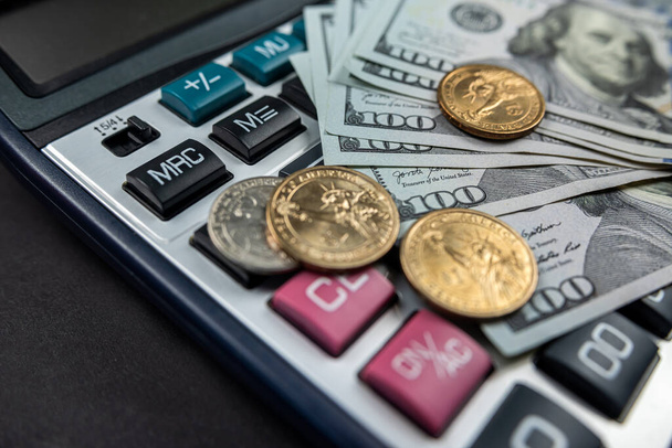 új számológép és dollárszámlák, fekete háttérrel elszigetelt érmékkel. Dollár árfolyam. Válság. finanszírozás - Fotó, kép