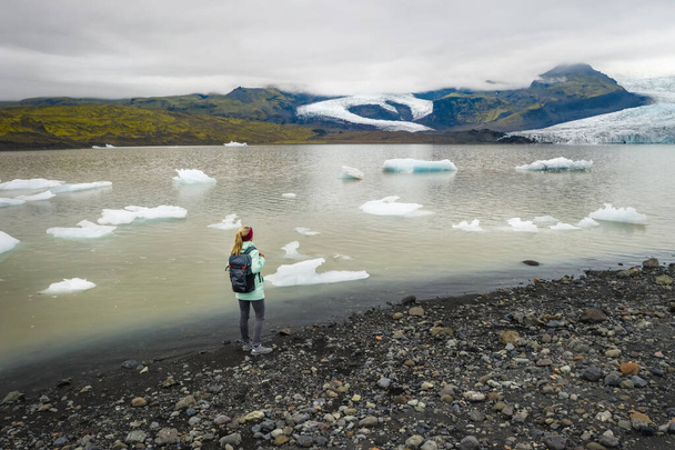 Woman traveler in scenic landscape at Fjallsarlon glacier lagoon in Iceland, with blue sky and moutain, in Vatnajokull National Park. - Photo, image