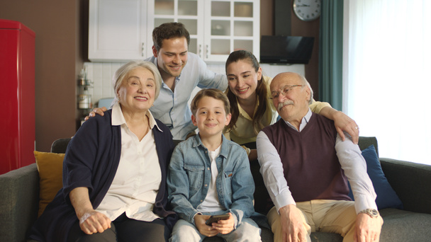 Молодая пара с детьми, их сын и пожилые родители сидят на диване в гостиной, фотографируют вместе. Портрет счастливой веселой большой семьи, улыбающейся на камеру в уютной гостиной. - Фото, изображение