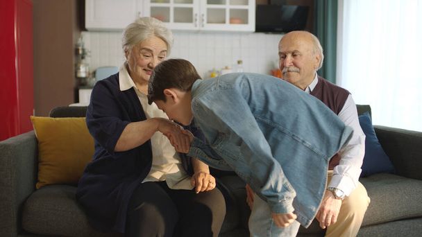 Хлопчик відвідав дідуся і відсвяткував Ейда аль-Фітра, поцілувавши їх руки. Щаслива старша пара сидить на дивані цілуючись і обіймаючи свою маленьку онуку..  - Фото, зображення