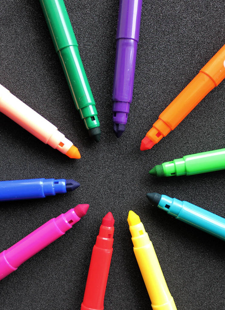 Open felt-tip pens of different colors in the shape of a star lie on a black background vertical photo  - Photo, Image