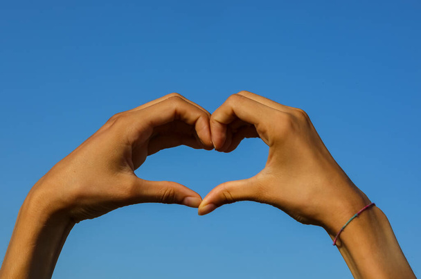 deux mains jointes formant la forme d'un cœur et le ciel bleu en arrière-plan - Photo, image