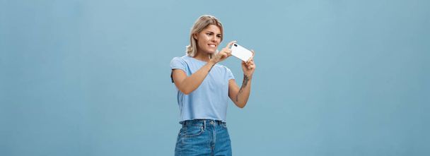 Lány próbál fotózni kisállat mozog gyorsan bámult intenzív okostelefon képernyő mutató telefon kamera bal érzés összpontosított, miközben a kép a mobiltelefon kék háttér. Technológia és - Fotó, kép