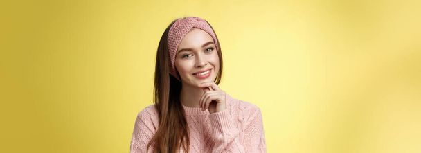 Счастливая молодая европейская женщина в трикотажном повязке, свитер наклоняя голову касаясь подбородка и улыбаясь глупо, заботясь о коже, чувствуя блестящими лица глядя чистый и здоровый после лечения кожи. - Фото, изображение