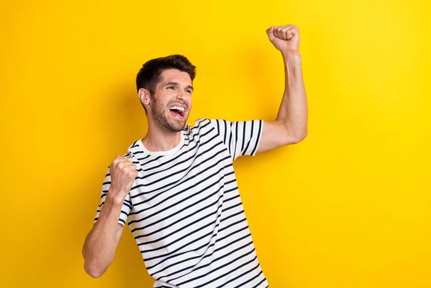 Photo of young positive man wear striped t-shirt fists up celebrate his favorite football club win competition isolated on yellow color background. - 写真・画像