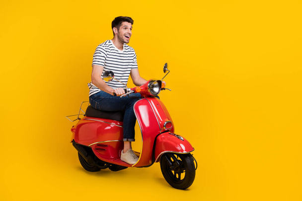 Full length photo of carefree excited man wear white t-shirt driving bike looking empty space isolated yellow color background. - Фото, зображення