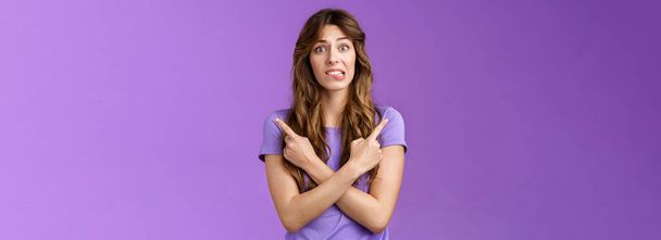 Perplexed timid hesitant worried girlfriend afraid making bad choice cross hands pointing sideways indicating left right perplexed decide frowning pull hesitant face asking advice purple background - Foto, Imagen