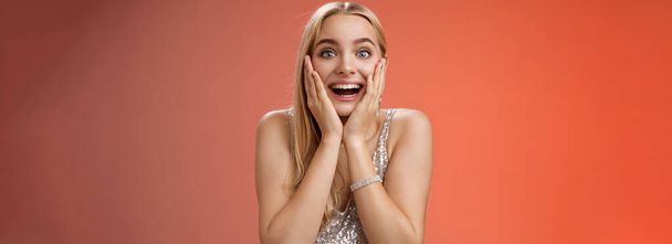 Amazed speechless excited attractive young woman blond long hair press palms cheeks blushing amused cannot believe see popular super star glancing thrilled amazement, surprised red background. - Фото, изображение