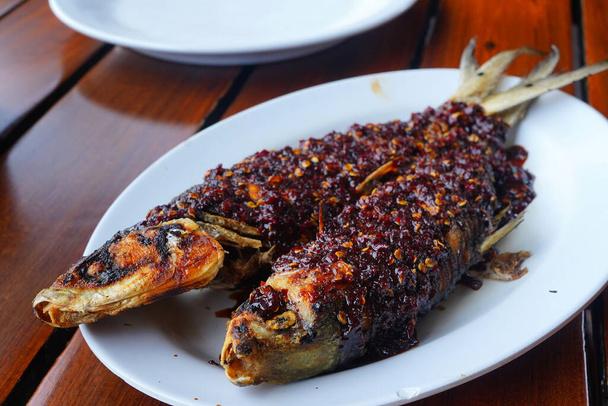 Жареная молочная рыба, покрытая острым чили-соусом и креветками, подается на белой тарелке. - Фото, изображение