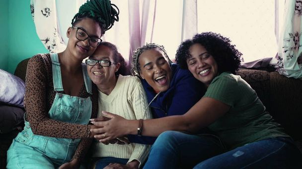 Happy Brazilian women hugging together. Joyful South American latin people embrace. Adult daughters hugging mature mother indoors 2 - Photo, Image