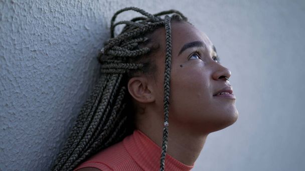 Eine junge schwarze Frau schließt die Augen, lehnt an der Wand. Erwachsene Mädchen mit Zöpfen Frisur ruht mit geschlossenen Augen - Foto, Bild