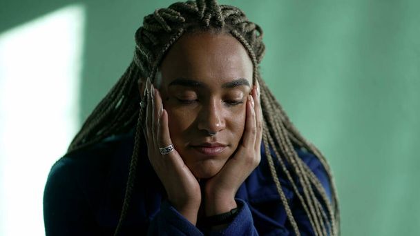 One pensive young black woman in contemplation. Thoughtful African American pensive adult girl with dreadlocks closeup face - Фото, изображение