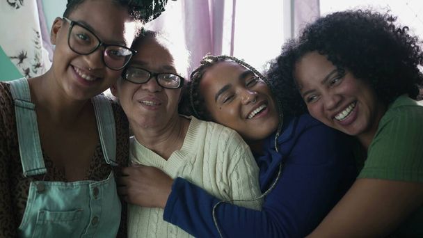 Happy Brazilian women hugging together. Joyful South American latin people embrace. Adult daughters hugging mature mother indoors - Photo, Image