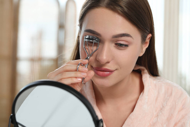 Woman using eyelash curler near mirror indoors - Fotografie, Obrázek