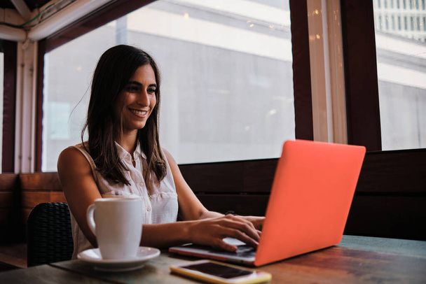 Mulher alegre feliz trabalhando com um laptop sentado em uma cafetaria - Foto, Imagem
