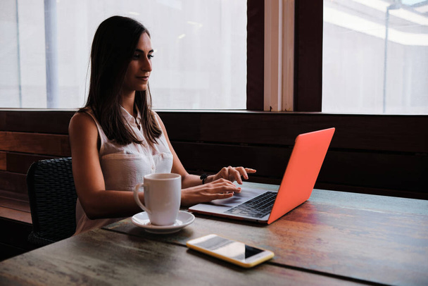 Πορτρέτο μιας επιχειρηματία ομορφιάς που εργάζεται με ένα φορητό υπολογιστή, ενώ πίνοντας έναν καφέ σε μια καφετέρια - Φωτογραφία, εικόνα