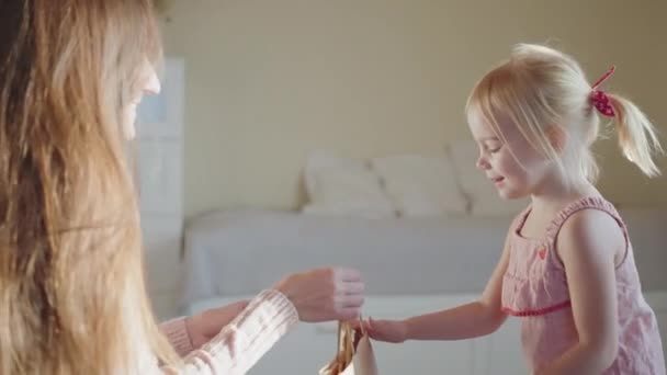 Jonge moeder geeft haar dochter een geschenk in milieuvriendelijke verpakking, het opgewonden meisje accepteert het geschenk. Happy Childhood Concept, ouderschap, recycleerbaar papier, eco-trend, ambachtelijk papier. 4k slow motion - Video