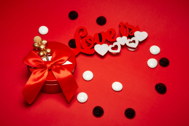 Punainen pyöreä laatikko, jossa on keula ja koristelu, kaiverrus rakkaus on valkoinen sydän, valkoinen ja musta pyöreä kiiltävä kiviä punaisella taustalla. - Valokuva, kuva