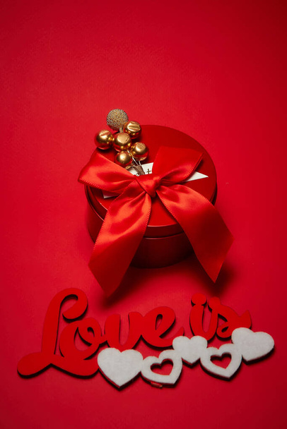 Punainen pyöreä laatikko, jossa on jousi ja merkintä rakkaus on valkoisilla sydämillä punaisella taustalla. Lähemmäs. Pystysuora laukaus. Näkymä ylhäältä. - Valokuva, kuva