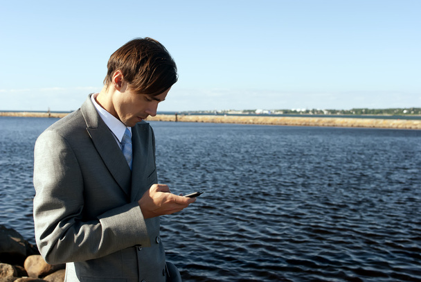 Man in a gray suit dials the phone against the sea - 写真・画像