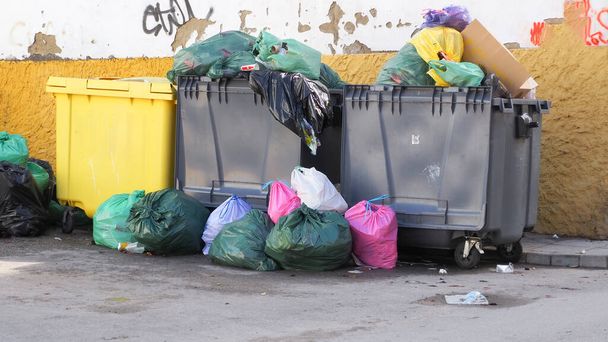 Müllcontainer mit Müll völlig verstopft gegen schmutzige Wand. - Foto, Bild